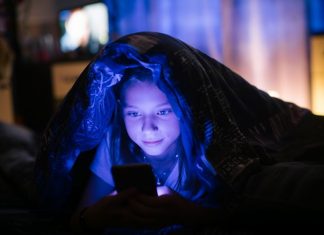 Little girl in bed under a blanket looking at the smartphone at night.